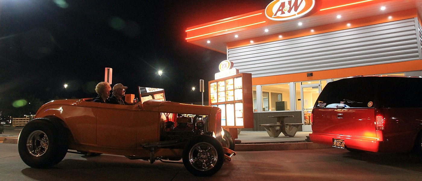 Two cars in A&W Restaurant drive-thru during the nighttime. 